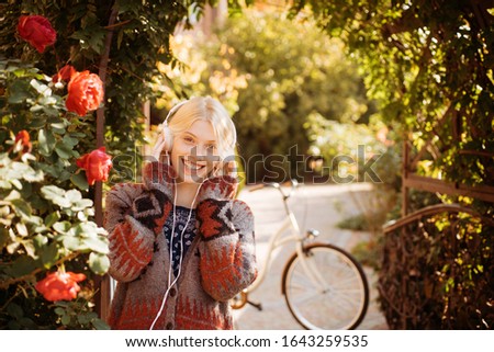Cheerful smiling woman at autumn park with bicycle at beautiful nature background. Blonde happy girl is listening to music outside. Close-up portrait of romantic dreamy female