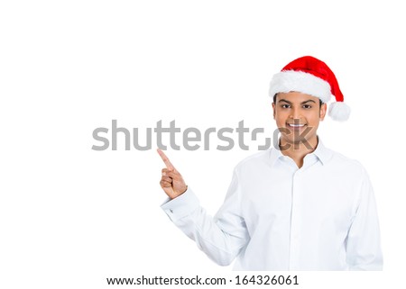 Closeup portrait of handsome young man wearing red santa claus hat pointing with index finger to space at left, isolated on white background. Positive human emotion facial expression.