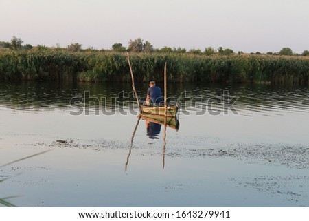 A fisherman in the middle of the river is fishing in a boat.
