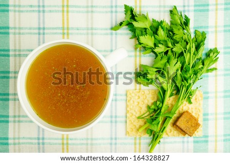 Bouillon, broth, clear soup in a white cup with a loaf, parsley, boiled egg on the tablecloth. Close-up.