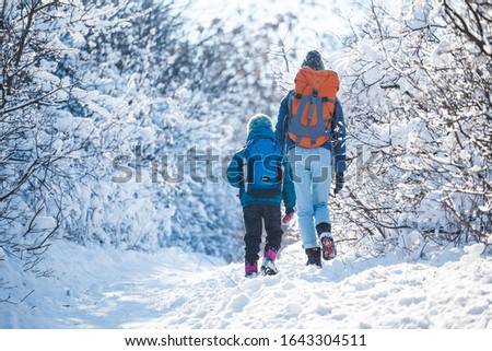 Woman with a child on a winter hike in the mountains. The boy travels with mother in the cold season. A child with a backpack walks with mother in a snowy park. Trekking with children. Winter trip. Royalty-Free Stock Photo #1643304511