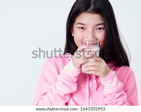 Portrait of healthy teenage girl drinking a glass of milk while standing on white background.