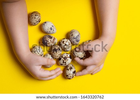 Kids hands holding many quail eggs on light yellow background. Concept of organic product. Top view