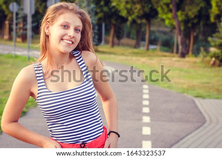 Beautiful smiling blonde girl outdoors. A teenager in casual style summer. Young woman in red pants and striped top