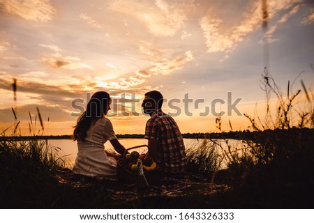 Silhouette of man and woman at sunset. Loving couple, girl and boyfriend, on a romantic date, on the riverbank