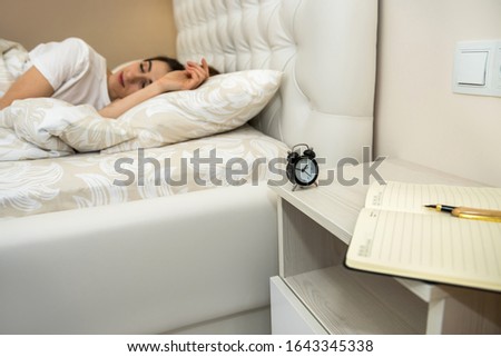 alarm clock on table and woman sleeping in background. Healthcare and sleep concept