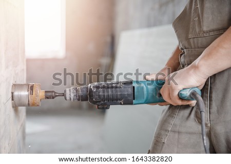 Builder man cutting electrical chase in concrete wall with hammer drill diamond crown.