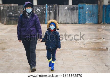 Mother and son walk down the street in protective face masks. Quarantined in city. Family wearing protective mask against transmissible infectious diseases and as protection against the flu outdoor.