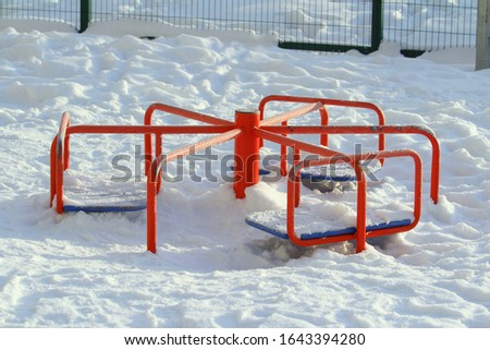 Children's red metal carousel covered with snow. Concept of entertaining street leisure for children, improvement of the urban environment. Stock photo with empty space for text.