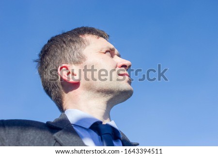 a middle-aged businessman man looking up into the sky with a serious and brooding facial expression on a sunny day