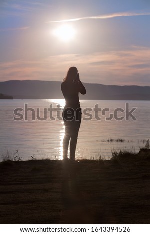 Girl with a camera photographs the sunset over the lake