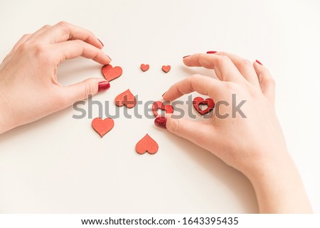 Woman hand touches red wooden hearts on the white table. St Valentine's Day. 8 March