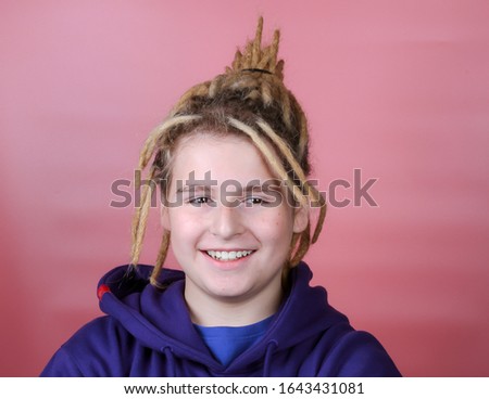 Smiling teenage boy with dreadlocks on a pink background
