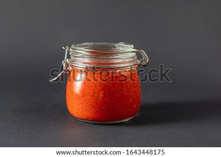 Hot chili pepper sauce paste harissa. Adjika. Traditional Tunisia, Georgian and Arabic cuisine. Homemade rose harissa in a glass jar on a black background. Side view, copy space.