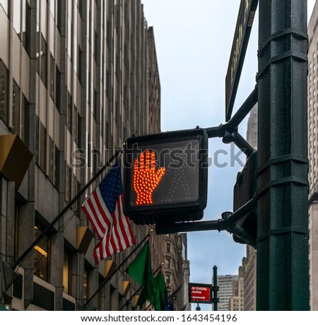 A pedestrian crossing signal for stopping on Fifth Avenue in New York with the American flag in the background