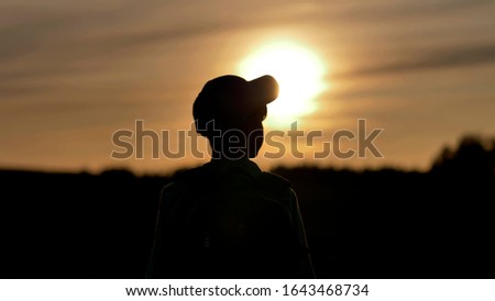 silhouette of a boy with backpack walking at sunset outdoors, travel concept