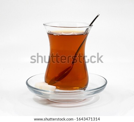 Traditional Turkish Tea glass filled with Black Tea isolated on white background.  Glass of Turkish tea with sugar cubes and teaspoon. Royalty-Free Stock Photo #1643471314