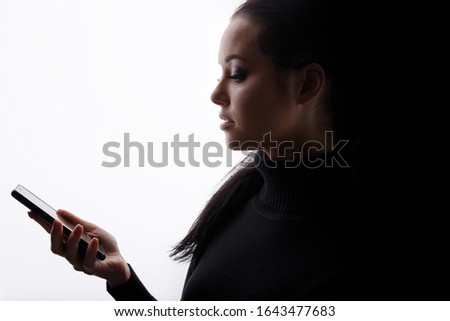 Beautiful young woman in a black dress with phone in her hand. Girl browsing internet on smartphone. White background. Free space for text.