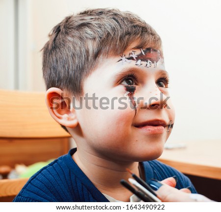 little cute child making facepaint on birthday party, zombie Apocalypse facepainting, halloween preparing concept, lifestyle people