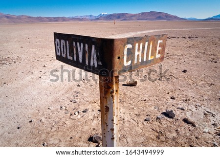 Old sign indicating border between Bolivia and Chile, with traveler's road behind