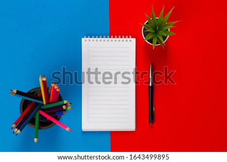 Colored pencils, notebook, pen, flower on a blue-red background. Make up.