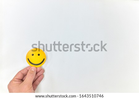 A hand holding a yellow smiling face on a white background with copy space. Positive feedback, good service and satisfied customer concepts.