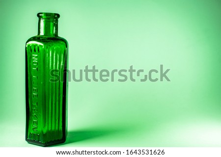 Green victorian home use chemicals bottle, Not to be taken sign, vintage glassware oldtimes common household item on green background with copy space