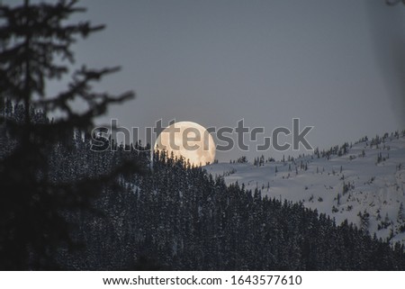 A picture of the moon peeking out from behind some mountains.   Whistler BC Canada
