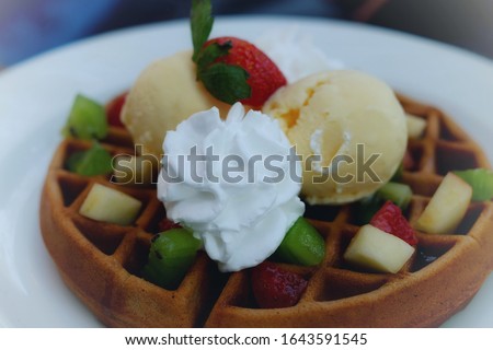 A plate of healthy dessert containing a round waffle served with icecream, whip cream and assorted minced fruits. 
