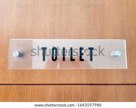 clear board with toilet sign attached to the wooden toilet door
