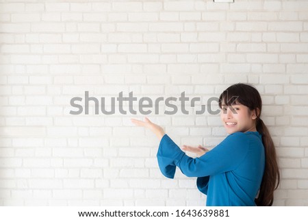 Beautiful young asian woman standing and smiling happy and presenting something and showing future or planning with message of you on cement concrete background, lifestyle concept.