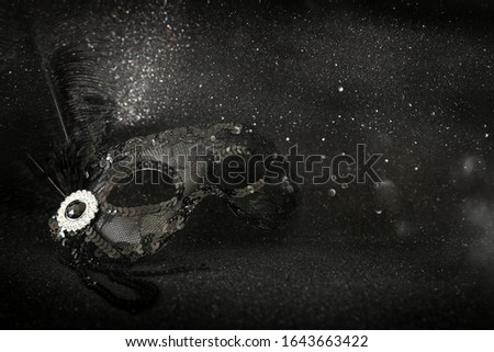 Photo of elegant and delicate black Venetian mask over dark glitter background