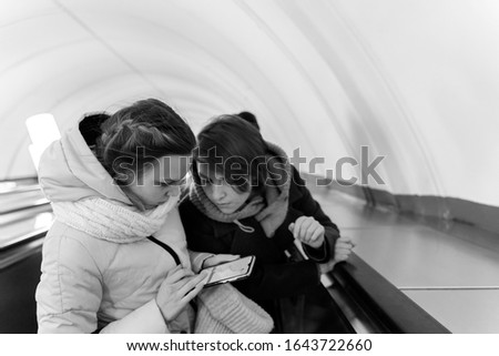 batman and a young girl on the escalator are looking at the smartphone. black and white photo