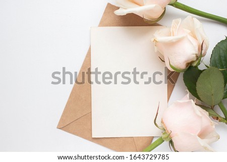 Minimalistic card mockup with roses. craft envelope, white flowers, branches, flat lay, top view. wedding invitation