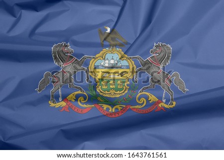 Crease of Pennsylvania fabric flag background. Coat of arms of Pennsylvania on blue field. The state of America.