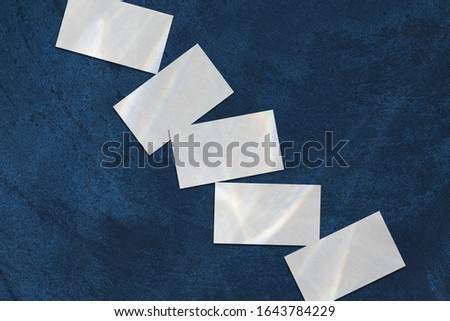 Close up of empty white rectangle business card mockups with overlay of water shadow and light caustic effect lying diagonally on dark blue concrete background. Flat lay, top view. Open composition.
