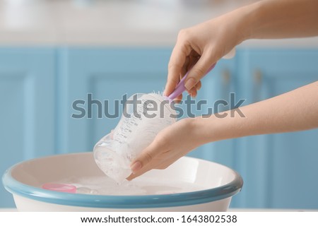 Woman cleaning baby bottle at home Royalty-Free Stock Photo #1643802538