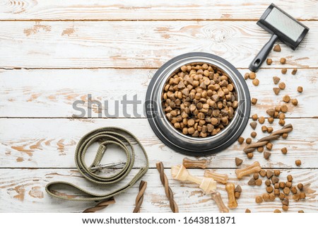 Bowl with dry pet food, dog lead and brush on white wooden background