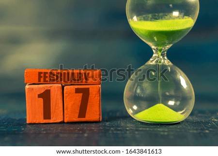 february 17th. Day 17 of month,Handmade wood cube with date month and day and hourglass with green sand. Time passing away. artistic coloring.  winter month, day of the year concept