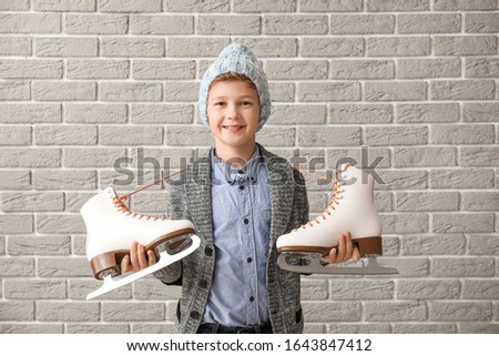 Cute little boy with ice skates against brick background