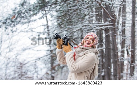 woman holding photo camera. taking picture in winter forest. Photographer photographing on snowy winter day. happy woman warm clothes fashion. winter travel vacation. stylish hipster traveler.
