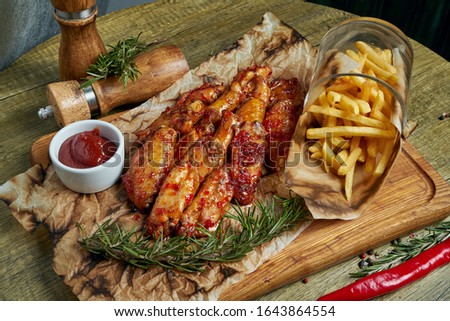 Great beer snack - spicy baked buffalo wings. BBQ wings with garnish of french fries on a wooden tray. Top view, food flat lay. Pub food