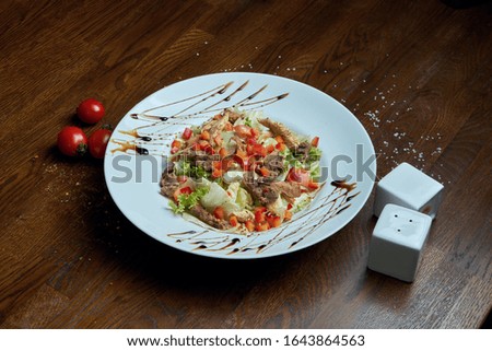 Healthy warm salad with grilled beef and vegetables on a white ceramic plate. Composition with salad and spices on a wooden background. Food photography
