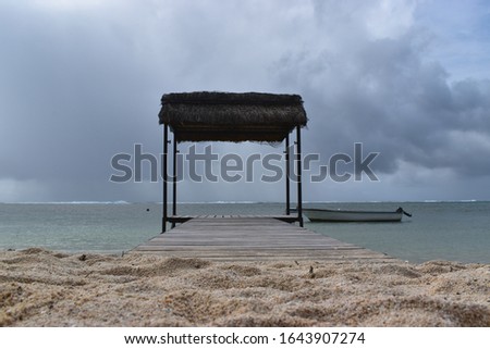 Picture of a beach and its white sand with in the background a beautiful hut on stilts and on the horizon a grey sky that heralds a tropical storm. Beautiful perspective.