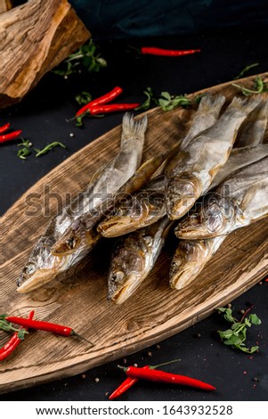 Dried salty pike fish on wooden board on black table background with chili.