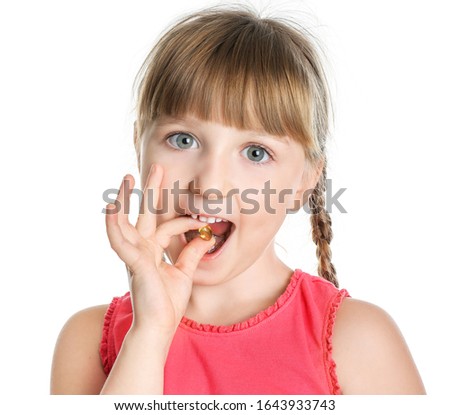 Little girl taking fish oil pill against white background