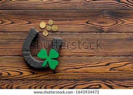 Composition for St. Patrick's Day.
Decorating paper with green clover or shamrocks, leprechaun hat and horseshoe.
Dark wooden background top view,flat lay, mockup