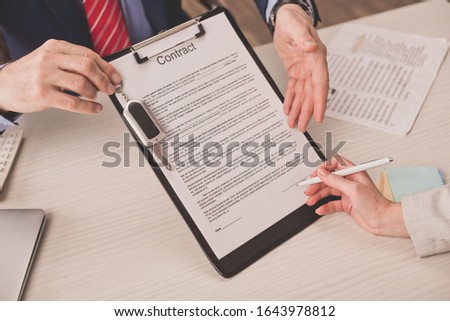 cropped view of agent pointing with hand at clipboard with contract lettering and car key near client