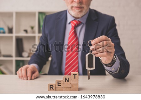cropped view of bearded agent holding car key near wooden cubes with rent lettering