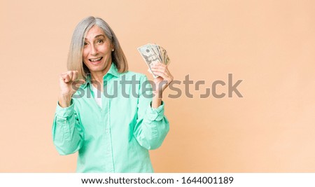 middle age pretty woman with dollar banknotes against copy space wall